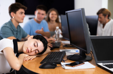 Fototapeta premium Exhausted students find solace in sleep, their heads resting on lecture hall desks during break.