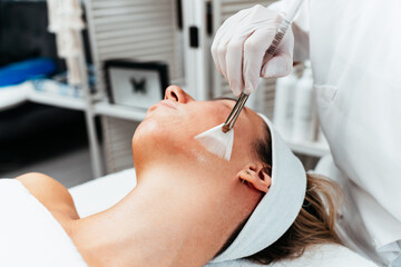 Professional beautician applying glycolic acid peel on face of beautiful young woman. Chemical...