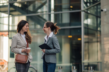 Fototapeta premium Two businesswomen talking and smiling outside office building