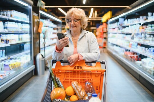 Happy senior woman looking at grocery store aisle with cellphone in hand