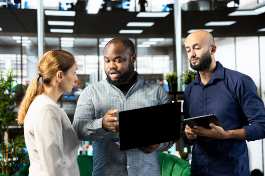 Manager looking at tablet screen with employee, showing him researching key data needed for finding business insights and finishing project task. Company executives analyzing data on device