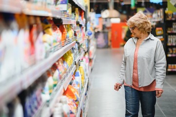 Elderly woman buying household chemicals or laundry detergent at supermarket.