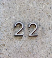 Metal street address number, number 22, mounted on a rough stone and concrete wall.