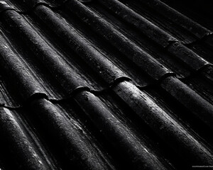 A close-up of aged, dark roof tiles, revealing their textured pattern and play of light and shadow.