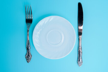 Empty white plate with fork and knife on blue background