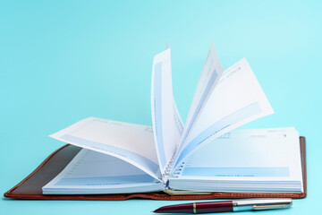 Open planner with flipping pages and a pen on a blue background