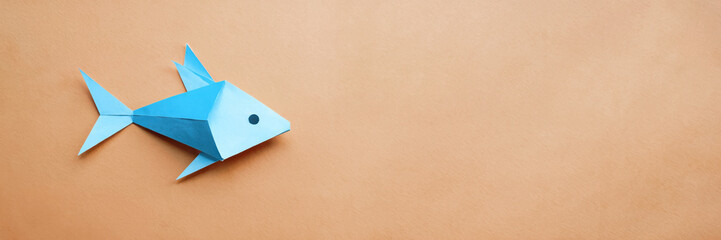 A fish is cut out of blue paper and placed on a orange background. "April Fools' Day" concept