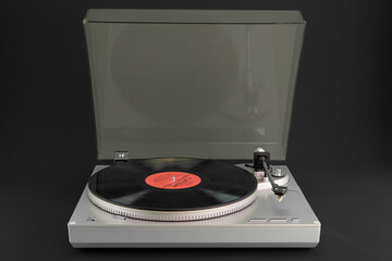 Vintage turntable with vinyl record and open dust cover on black background