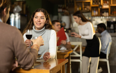 European woman happily chats with her husband while sitting in a cozy restaurant with a glass of wine. Romantic dinner for a couple in a European restaurant