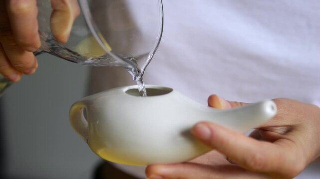 Healthcare professional pouring sterile water into ceramic neti pot, performing nasal irrigation technique targeting sinus congestion and respiratory wellness. concept of nasopharynx cavity hygiene