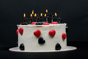 Birthday cake decorated with black candles shaped Happy Birthday inscription, hearts shaped jellies.