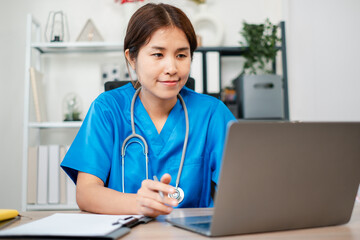 A female doctor in blue scrubs conducts an online consultation using a laptop in a modern medical...