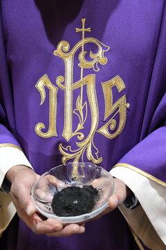 Ein r&ouml;misch-katholischer Priester h&auml;lt am Aschermittwoch eine Schale mit scharzer Asche. Der lilafarbene Talar, hat die Aufschrift: IHS. Iesus Hominum Salvator. Jesus, Erl&ouml;ser der Menschheit 