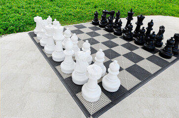 Giant outdoor chess set, white and black figurines on the board in the hotel garden for outdoor activity.
