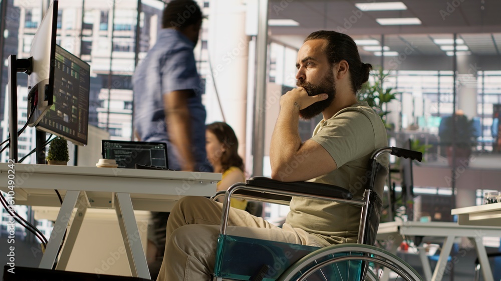 Poster it worker with disability sitting in wheelchair in office working at computer desk, focused on testi