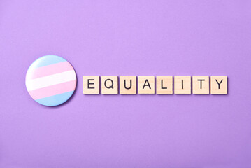 Wooden word Equality beside a trans flag badge, symbol of transgender community.