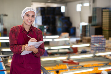 Diligent female worker takes inventory of ripe tangerines on a packing line.
