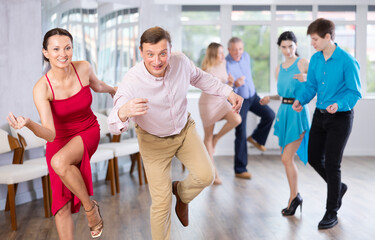 Group is of different ages active people engaged in Latin dance studio and learns movements of...