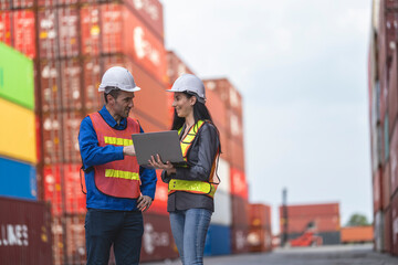 Two logistics workers man and woman discuss operations at a busy shipping container yard.