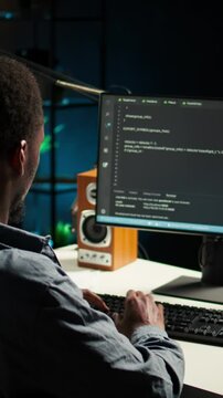 Vertical Video African american expert at desk using pc for programming and data analysis. Young networking expert working from his home setup, manages information technology and data center. Camera A
