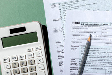 Close-up USA individual income tax return form 1040 and white calculator on green background