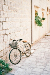 Fototapeta premium Lady bicycle with a basket on the handlebars stands near the stone wall of an old house