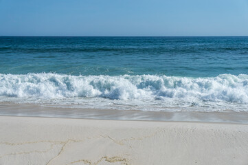 Small sized waves of Atlantic Ocean blue waters breaking on Praia Seca beach white sands shoreline...