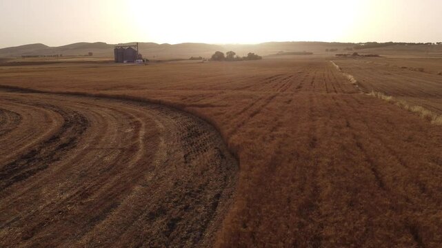 A sunset aerial view of a wheat field and silos in the countryside during summer harvest season in the hills of Beja in the north of Tunisia.