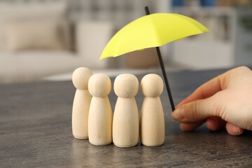 Woman holding umbrella over human figures at grey table indoors, closeup. Insurance concept