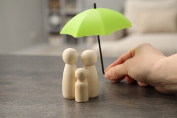 Woman holding umbrella over human figures at grey table indoors, closeup. Insurance concept