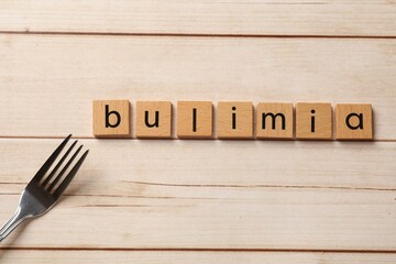 Word Bulimia and fork on white wooden table, top view