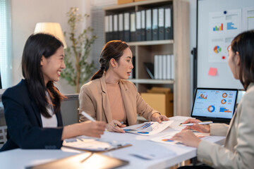 Three women are sitting at a table with papers and a laptop