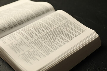 Fototapeta premium Open Holy Bible in English language on black table, closeup