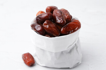 Tasty sweet dried dates in paper bag on white table, closeup