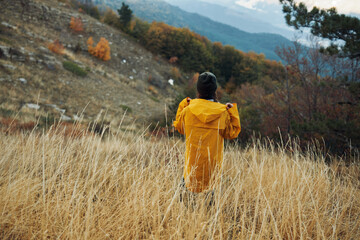 A solitary figure in a vibrant yellow raincoat standing among the tranquil beauty of a mountainous field
