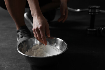 Woman applying talcum powder onto her hands above bowl before training in gym, closeup