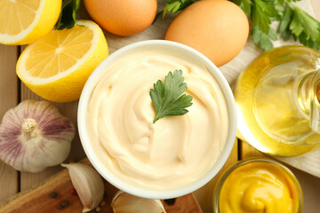 Delicious mayonnaise sauce in bowl and ingredients on wooden table, flat lay