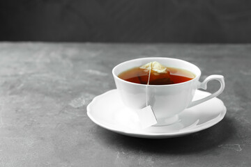 Tea bag in cup with hot drink on gray textured table. Space for text