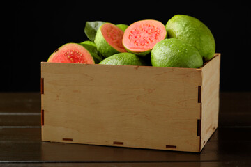 Fresh cut and whole guava fruits in wooden crate on dark table, closeup