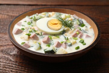 Delicious okroshka soup with kefir in bowl on wooden table, closeup