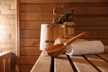 Ladle, towels, bucket and whisk on wooden bench in sauna. Space for text