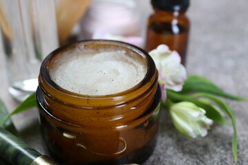 Body care products in jar and flowers on grey table, closeup