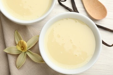 Tasty condensed milk, vanilla pods, flower and spoon on white wooden table, flat lay