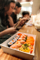 A plate of delicious assorted Japanese salmon sushi served as family favorite lunch menu at supermarket food court with teens and children sitting on the background