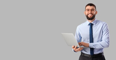 Handsome young happy businessman with laptop on grey background with space for text