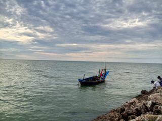 Fototapeta premium a calm sea view with a small boat floating in the middle. The boat is dark blue in color with red accents on the back.