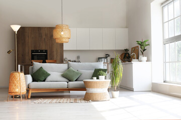 Interior of light living room with cozy grey sofa, coffee table and glowing lamps near big window