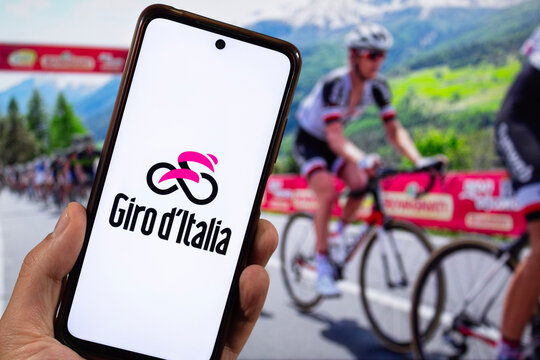 a male right hand with Giro d Italia bicycle race logo inside a smartphone with a bicycle competition at background
