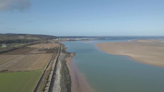 Aerial view of the estuary of the river Dee in the Aberdeen bay on a sunny day. Drone rotating to the right showing the blue water of the river and the sandy banks in the river mouth. Blue sky.