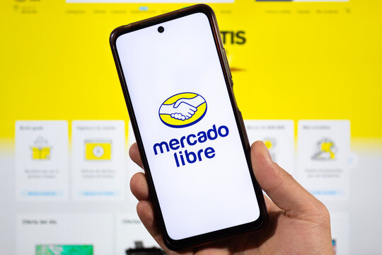 a male right hand with mercado libre logo inside a smartphone with mercado libre interface at background